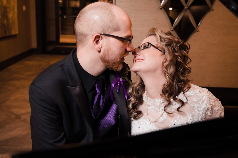 Bride and groom kiss while sitting at a piano at Innsbrook Country Club in Merrillville, IN