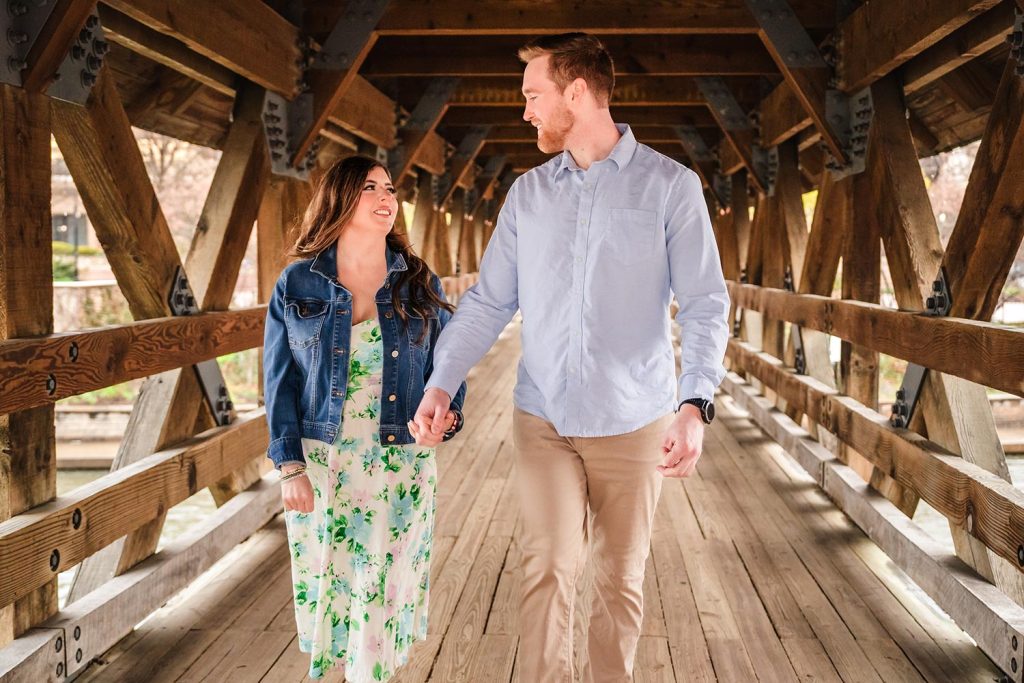 Engaged couple walking across the bridge at the Naperville Riverwalk in Naperville, IL