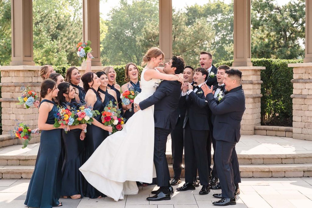 Wedding party celebrates as the groom lifts the bride during portraits at Chevy Chase Country Club and Traditions in Wheeling, IL