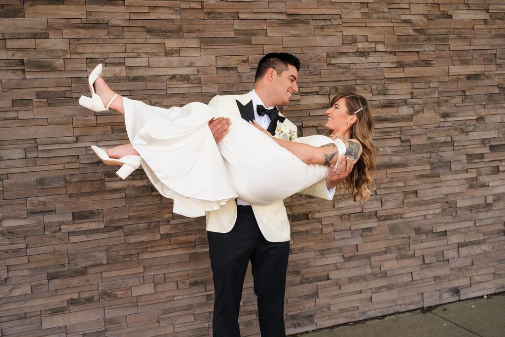 Groom lifts and smiles at bride during couples portraits outside their reception at Biagio Events in Chicago, IL