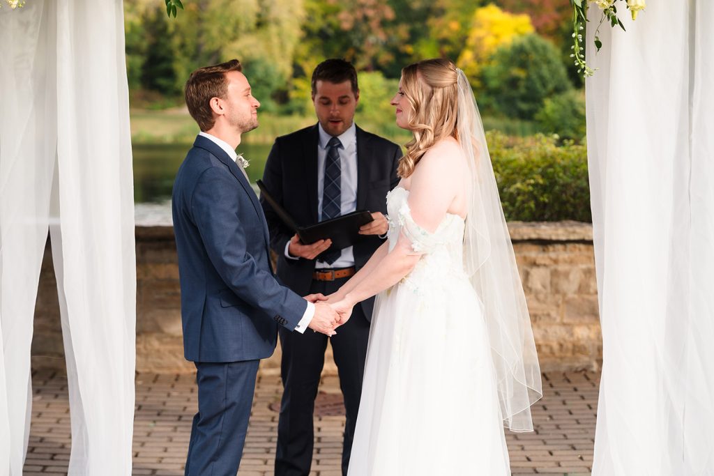 Bride and groom hold hands during their wedding ceremony at Lake Ellyn Boathouse in Glen Ellyn, IL